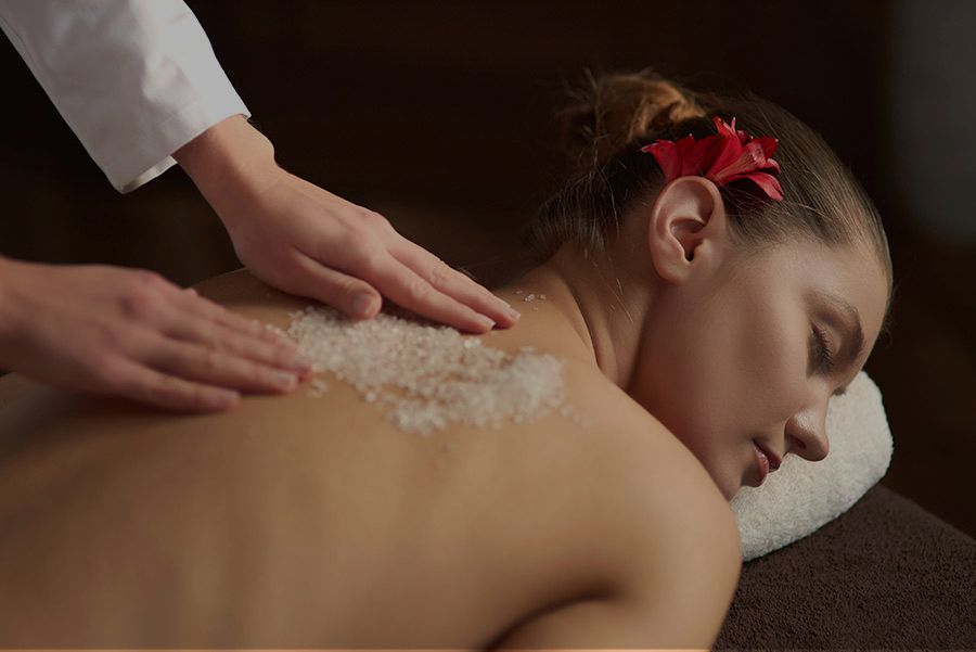 Spa therapist applying exfoliating treatment to client’s bac